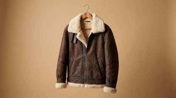Brown B6 bomber jacket in real shearling hanging on a wooden hanger against a tan background