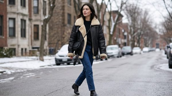 Woman wearing a womens sheepskin bomber jacket in black with a cream shearling collar on a snowy city street